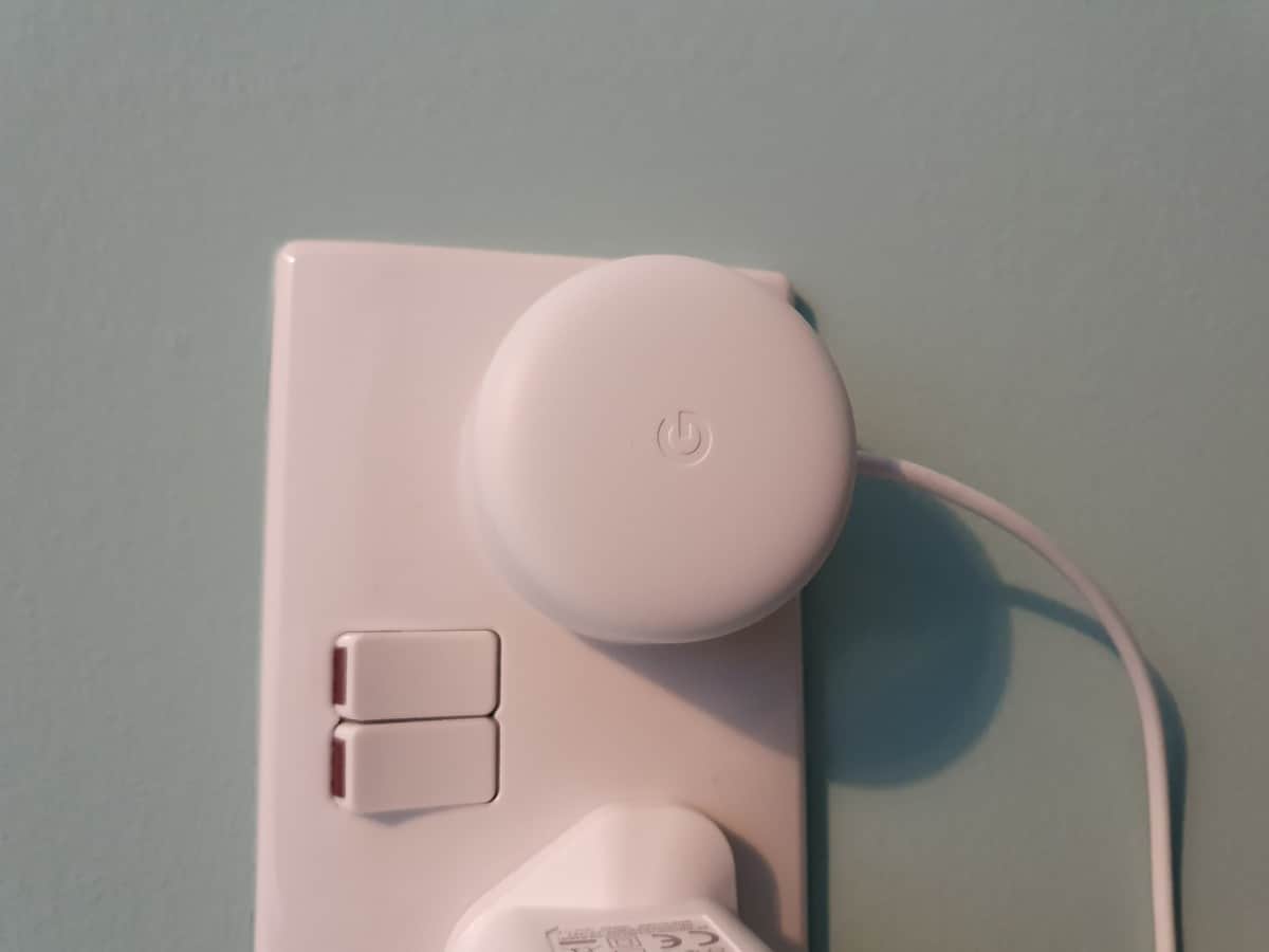 A Google Nest Mini power adapter, plugged into a UK wall socket.