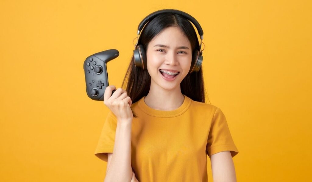 Asian woman in casual yellow t-shirt and playing video games using joysticks with headphones