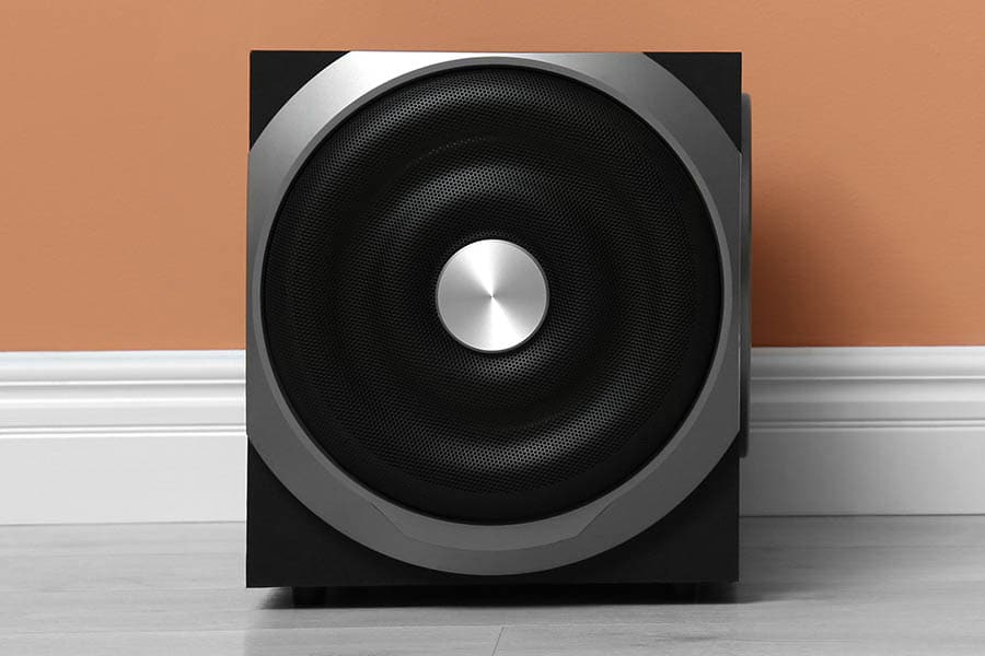 Modern powerful subwoofer on floor near orange wall