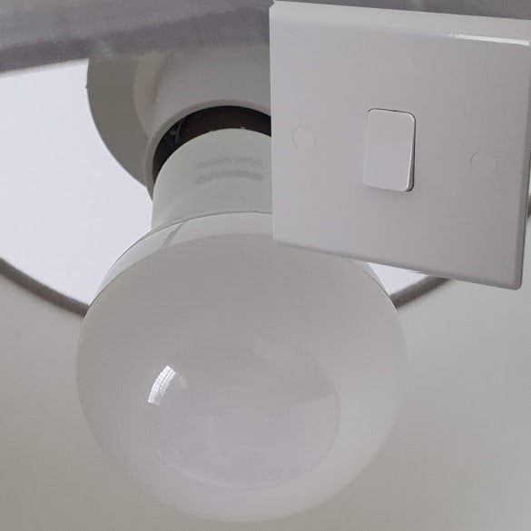 A Philips Hue White B22 bayonet bulb in the background, and an overlay UK light switch in the off position (in the foreground).