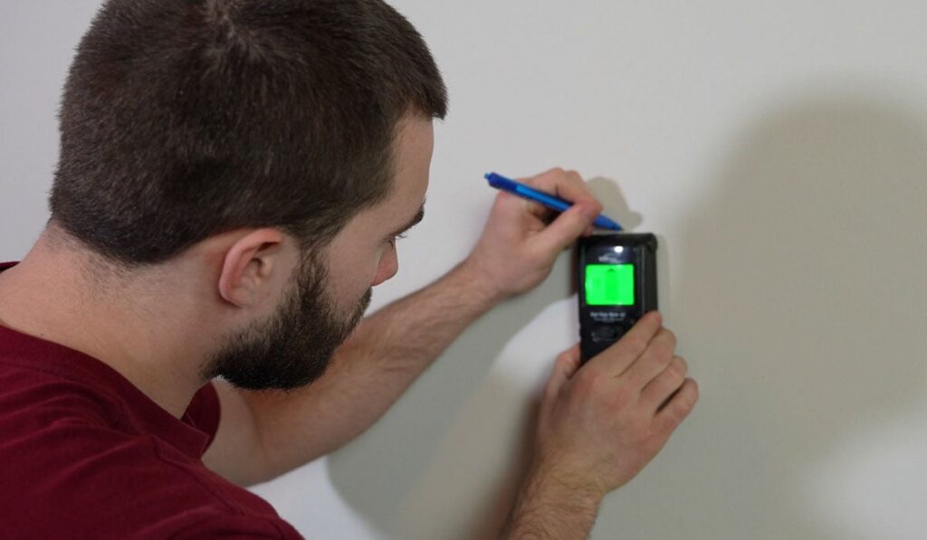 Man using a stud finder to mark studs on a wall