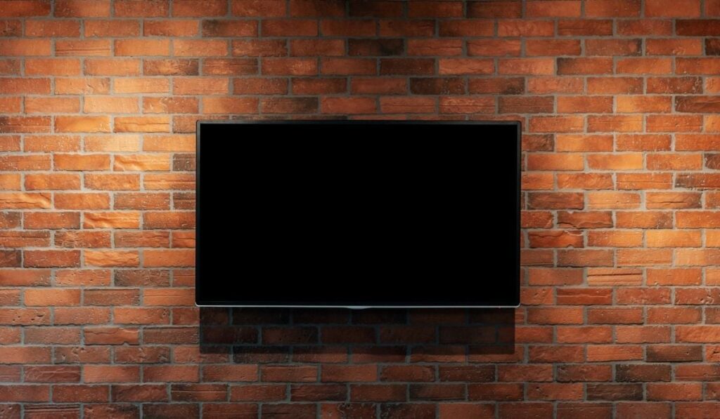 Modern TV with blank black screen, hanging on red brick wall