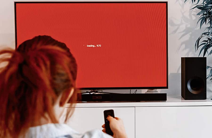 woman sitting in her living room and holding a TV remote control in front of a screen display waiting message