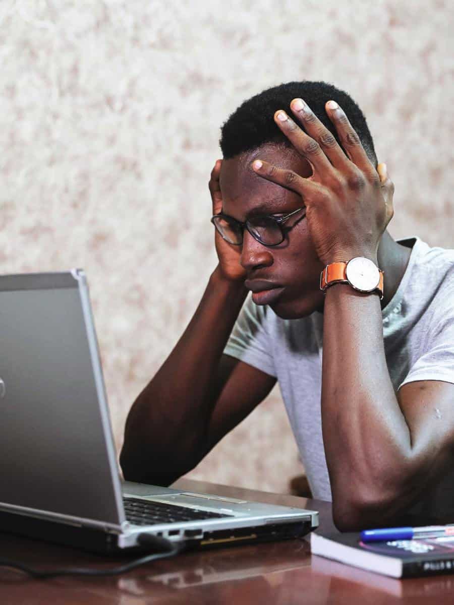 A frustrated man using a laptop, with his hands around his head.