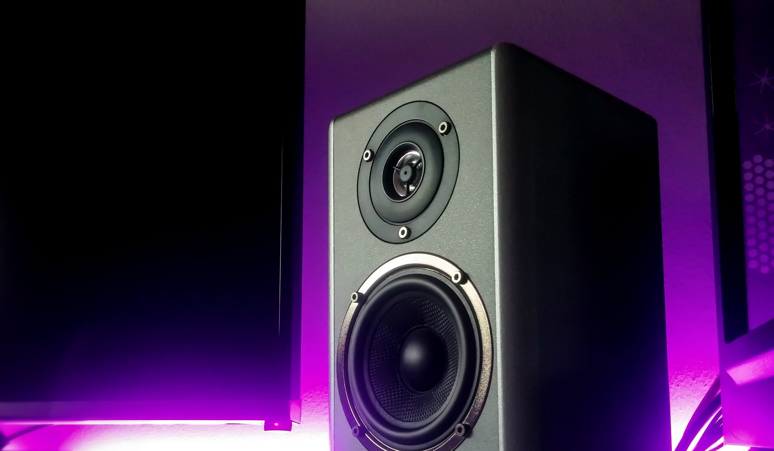 A speaker by a monitor, back-lit with a purple glow