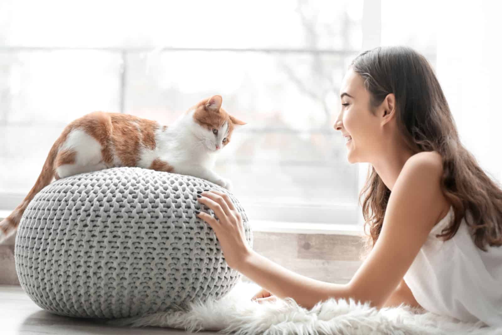 Beautiful young woman with cute cat near window at home