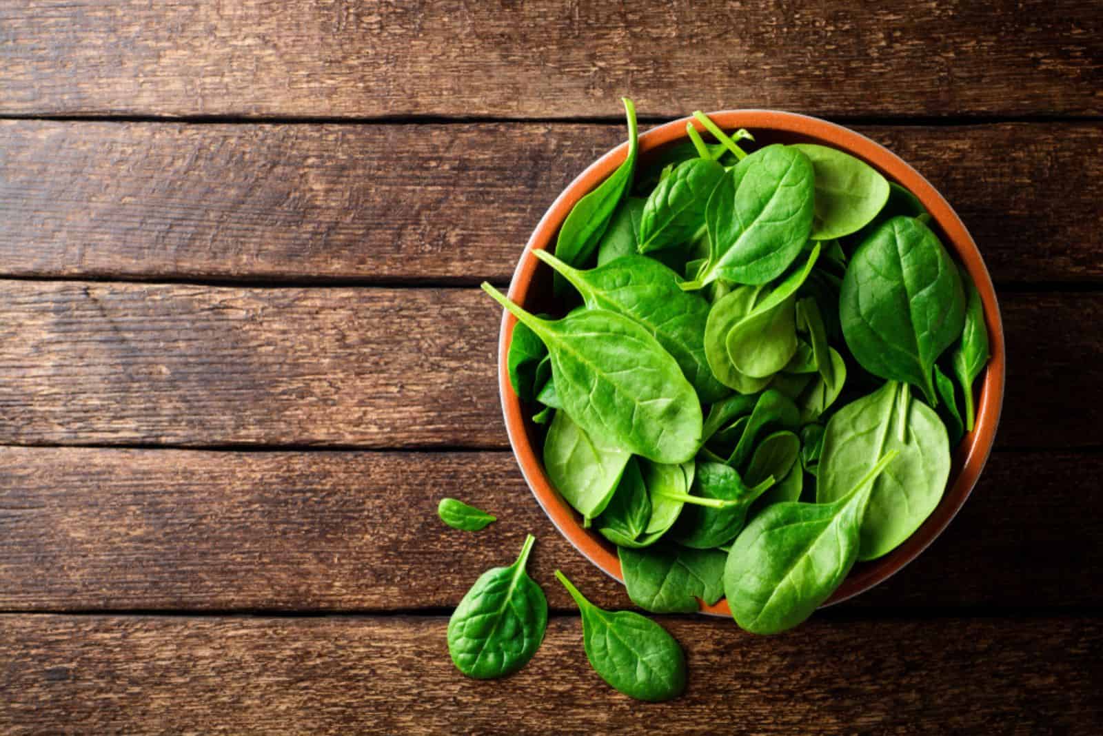 Fresh spinach leaves in bowl on rustic wooden table