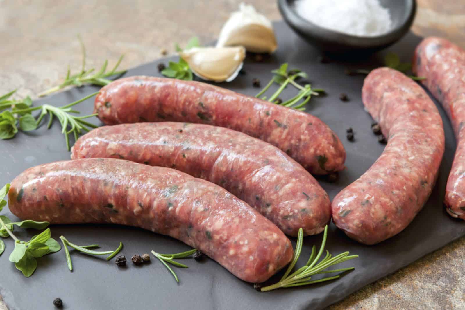 Raw sausages on slate, with herbs and spices