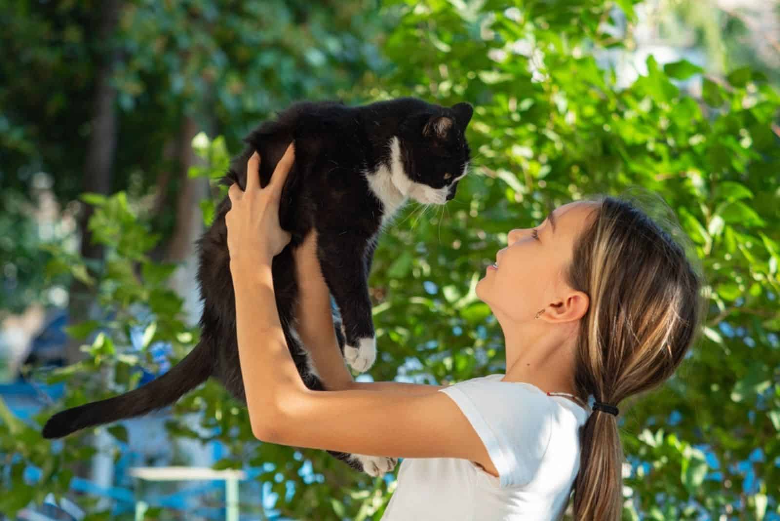 girl holds a black stray cat in her arms