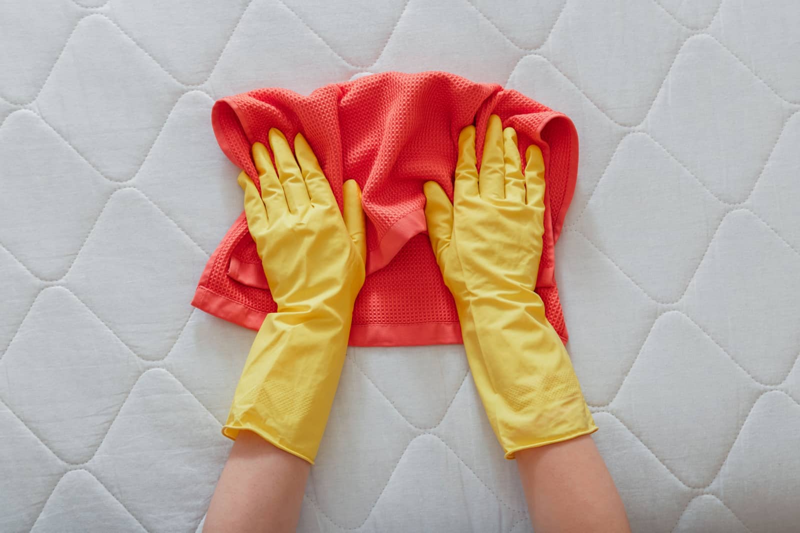 person cleans surface of mattress on bed with rag.