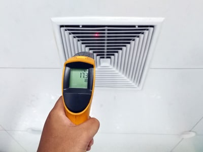 HVAC technician checking the temperature of an air supply register