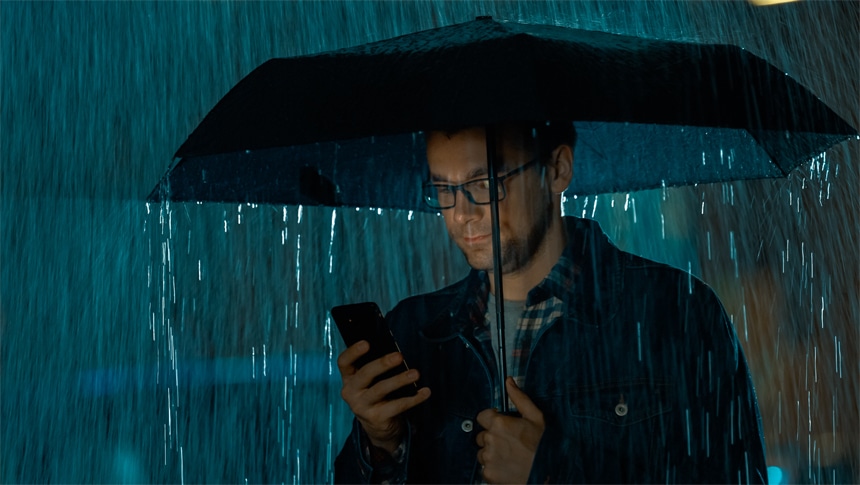 Man checking his phone under an umbrella in the rain